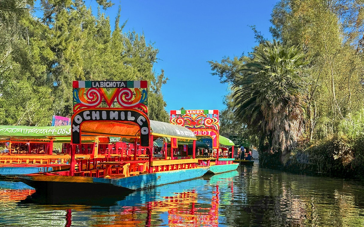 Trajinera boats on Xochimilco canal, Mexico City, with colorful decorations.