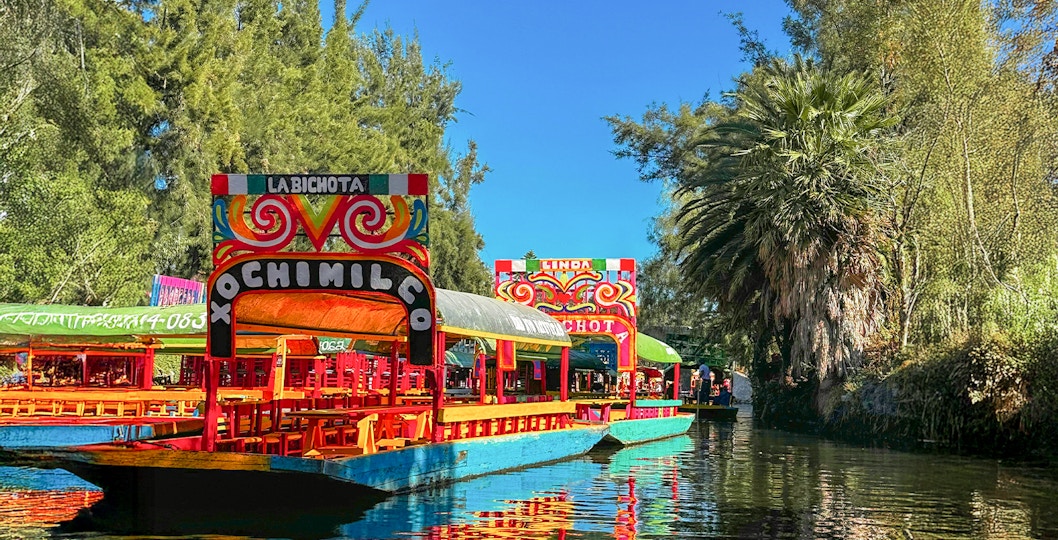 Trajinera boat with colorful decorations on Xochimilco canal, Mexico City, featuring lively group celebration.