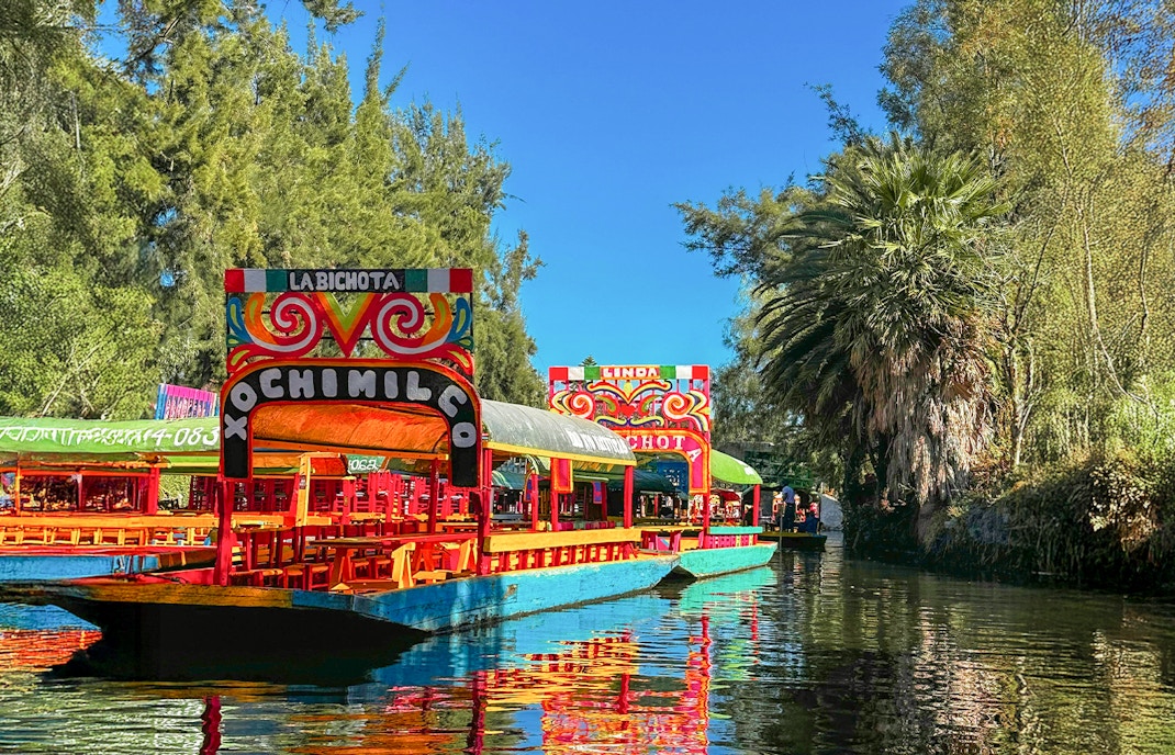Trajinera boat with colorful decorations on Xochimilco canal, Mexico City, featuring lively group celebration.