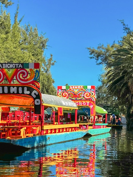 Trajinera boats on Xochimilco canal, Mexico City, with colorful decorations.