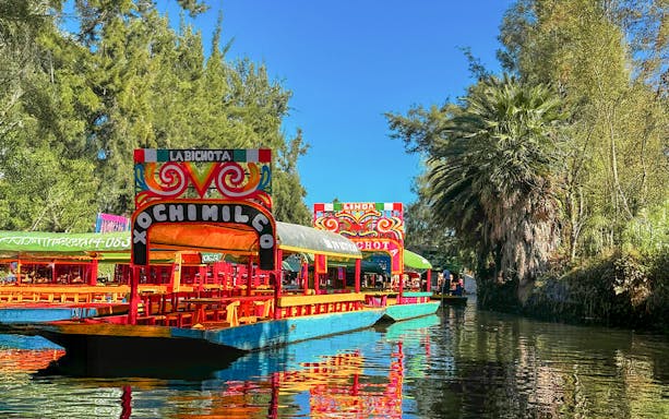 Trajinera boats on Xochimilco canal, Mexico City, with colorful decorations.