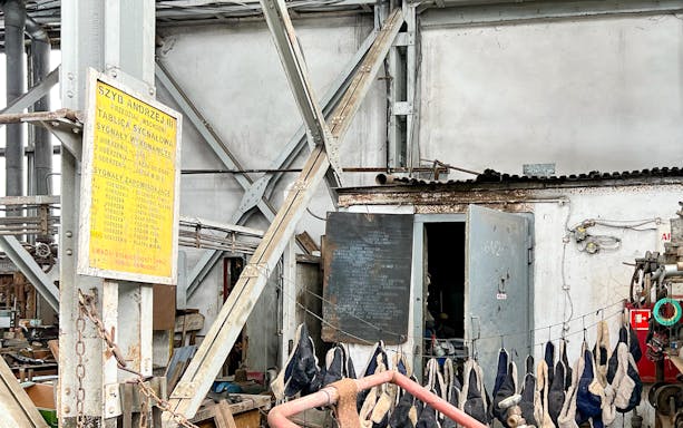 Industrial interior of Auschwitz sub-camp with machinery and hanging gloves, part of exclusive history tour.