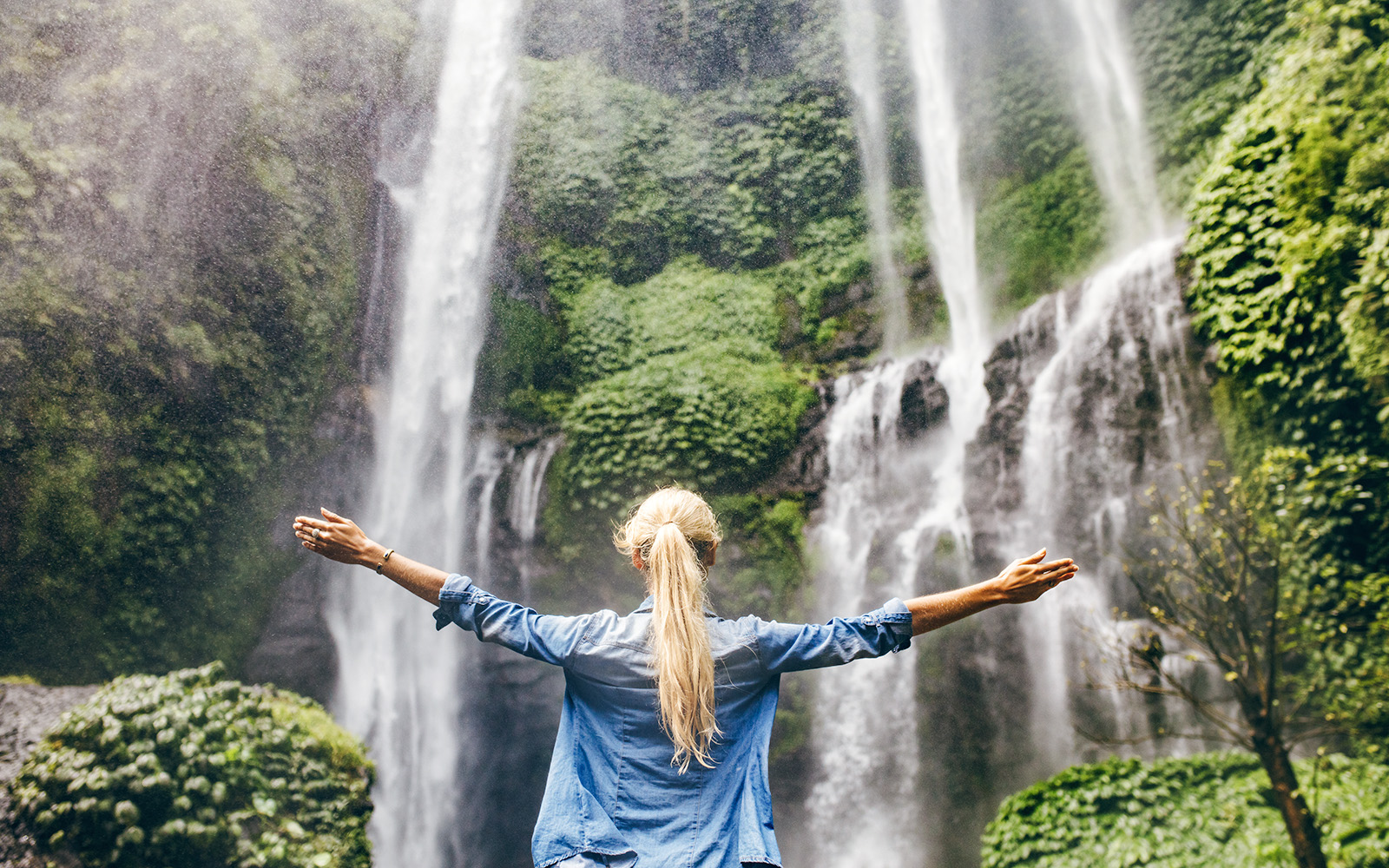 Person standing with arms outstretched in front of a waterfall on the Road to Hana, Maui, Hawaii.