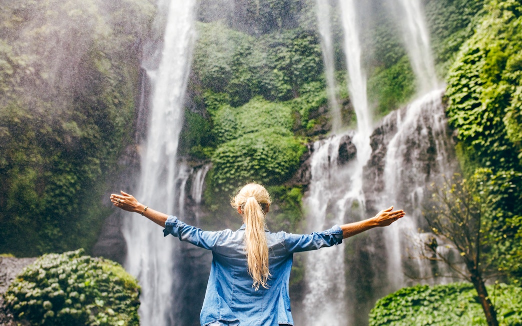 Person standing with arms outstretched in front of a waterfall on the Road to Hana, Maui, Hawaii.