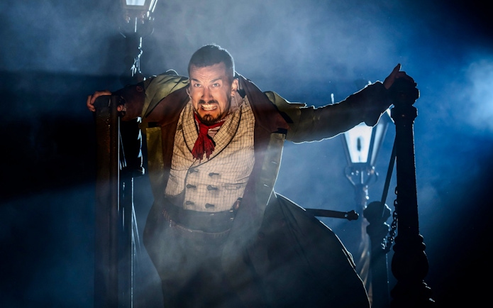 Actor in dramatic scene from Oliver production, gripping lamppost with intense expression.