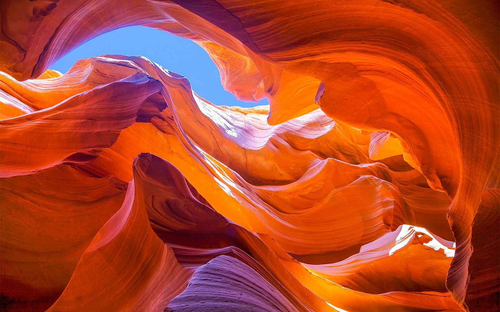 Antelope Canyon's swirling orange rock formations under a blue sky.