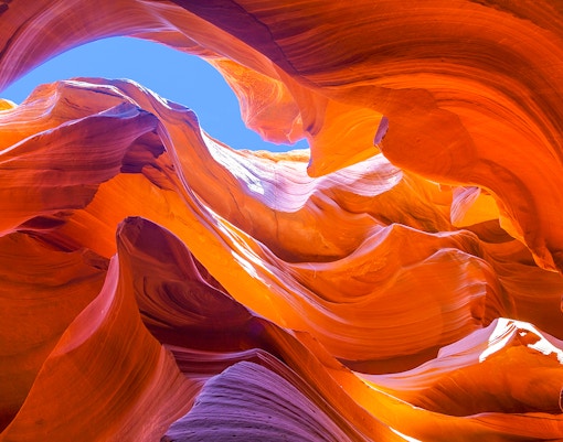 Antelope Canyon's swirling orange rock formations under a blue sky.