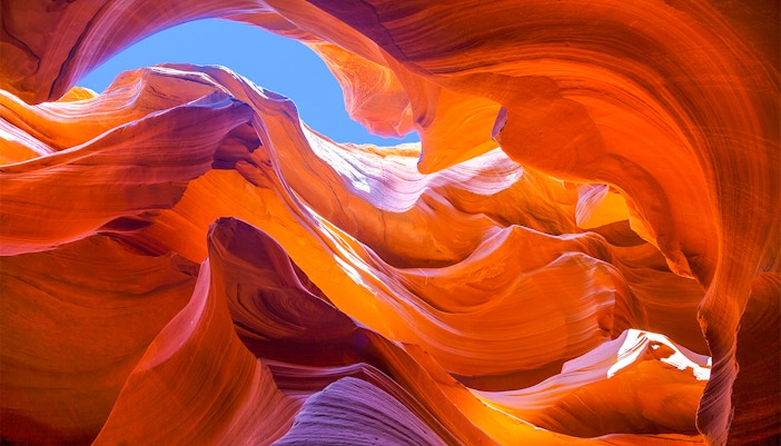 Antelope Canyon's swirling orange rock formations under a blue sky.