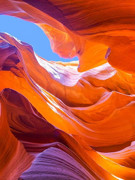 Antelope Canyon's swirling orange rock formations under a blue sky.