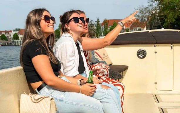 Tourists enjoying a Harlem canal cruise on an open boat, with one pointing at sights.