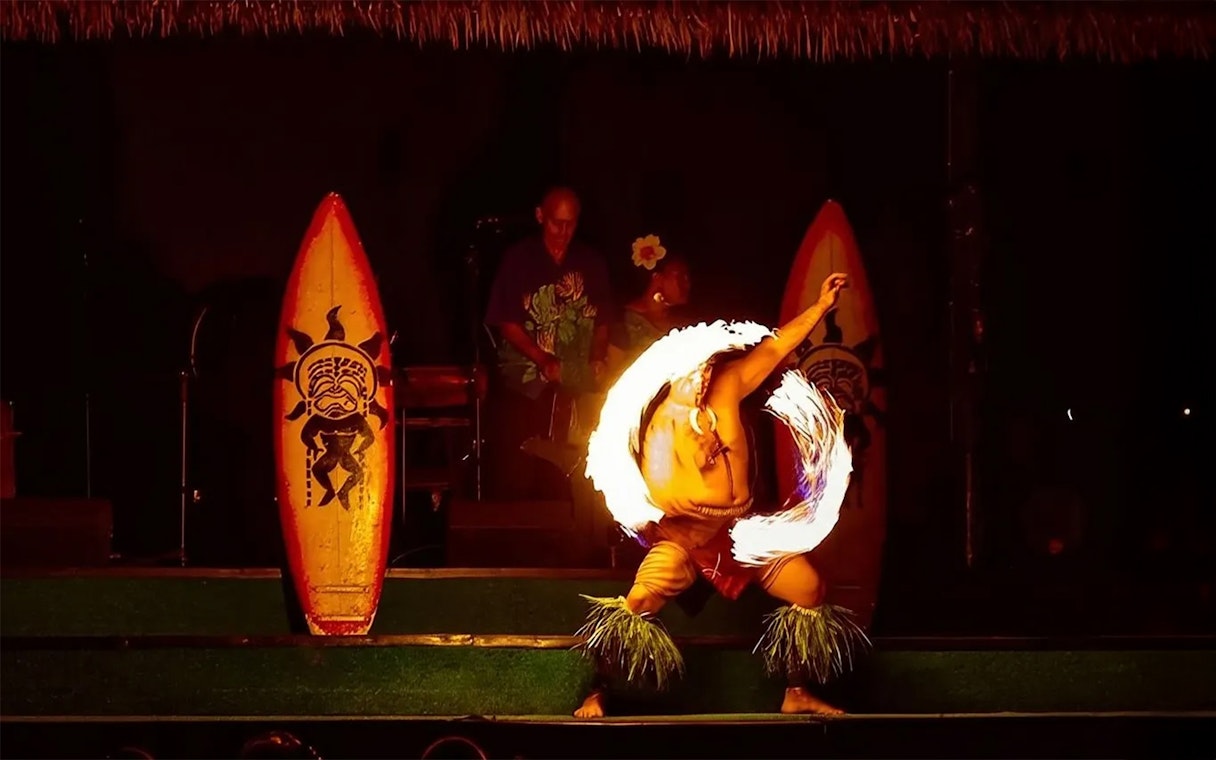 Fire dancer performing at Paradise Cove Luau, Hawaii with traditional surfboards in the background.