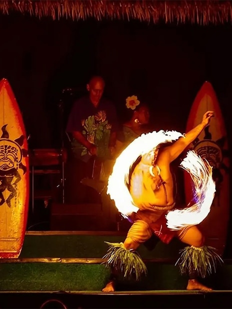 Fire dancer performing at Paradise Cove Luau, Hawaii with traditional surfboards in the background.