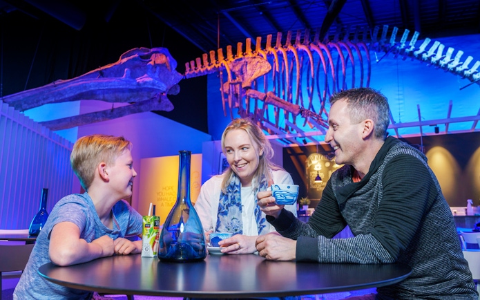 Family enjoying drinks under whale skeleton at Whales of Iceland Museum.