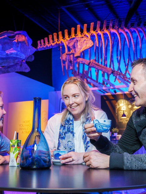 Family enjoying drinks under whale skeleton at Whales of Iceland Museum.