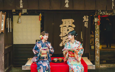Couple in kimonos enjoying tea outside a traditional Japanese shop.