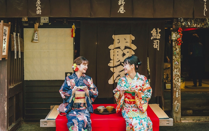 Couple in kimonos enjoying tea outside a traditional Japanese shop.