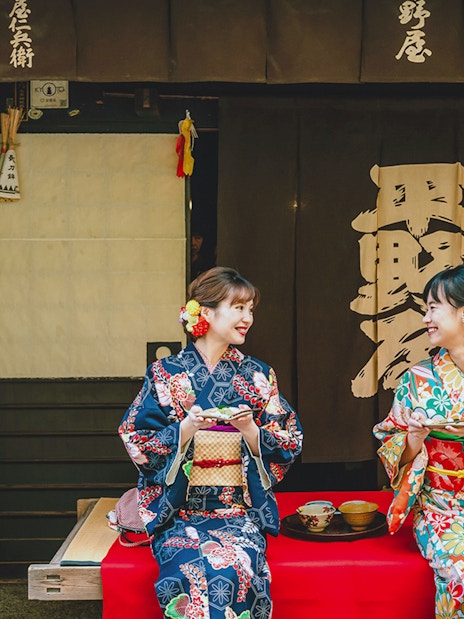 Couple in kimonos enjoying tea outside a traditional Japanese shop.