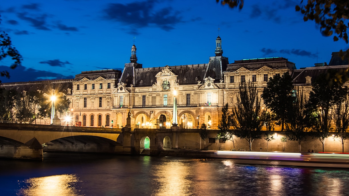 Louvre Museum illuminated at night viewed from Seine River cruise, Paris.