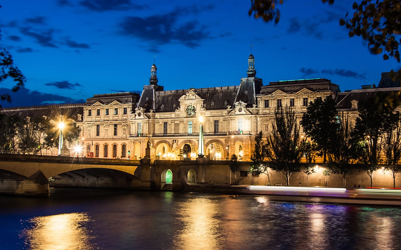 Louvre Museum illuminated at night viewed from Seine River cruise.