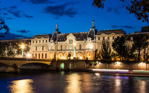Louvre Museum illuminated at night viewed from Seine River cruise.