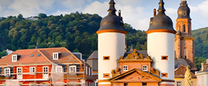 Old Bridge gate towers in Heidelberg, Germany, with historic buildings and hills in the background.