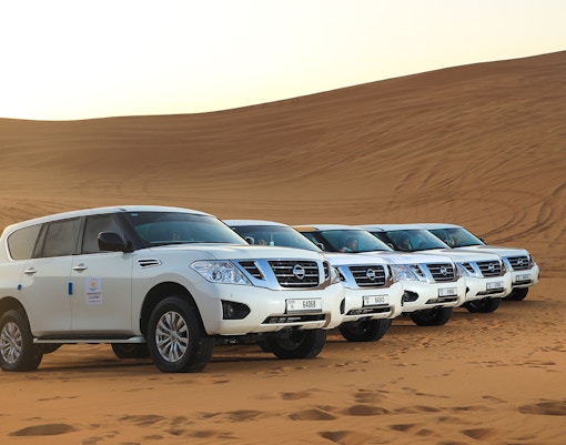 Four white SUVs parked on Arabian desert dunes for a premium safari experience.