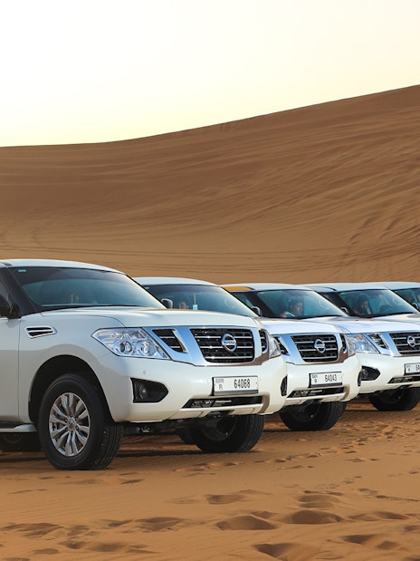 Four white SUVs parked on Arabian desert dunes for a premium safari experience.