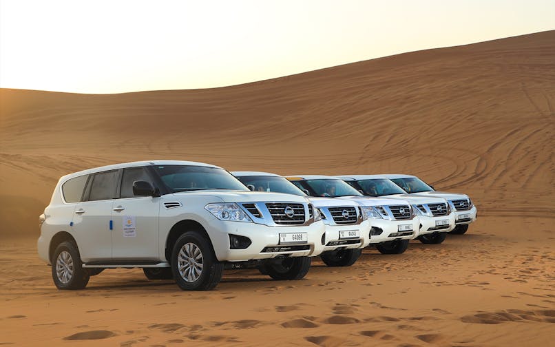 Four white SUVs parked on Arabian desert dunes for a premium safari experience.