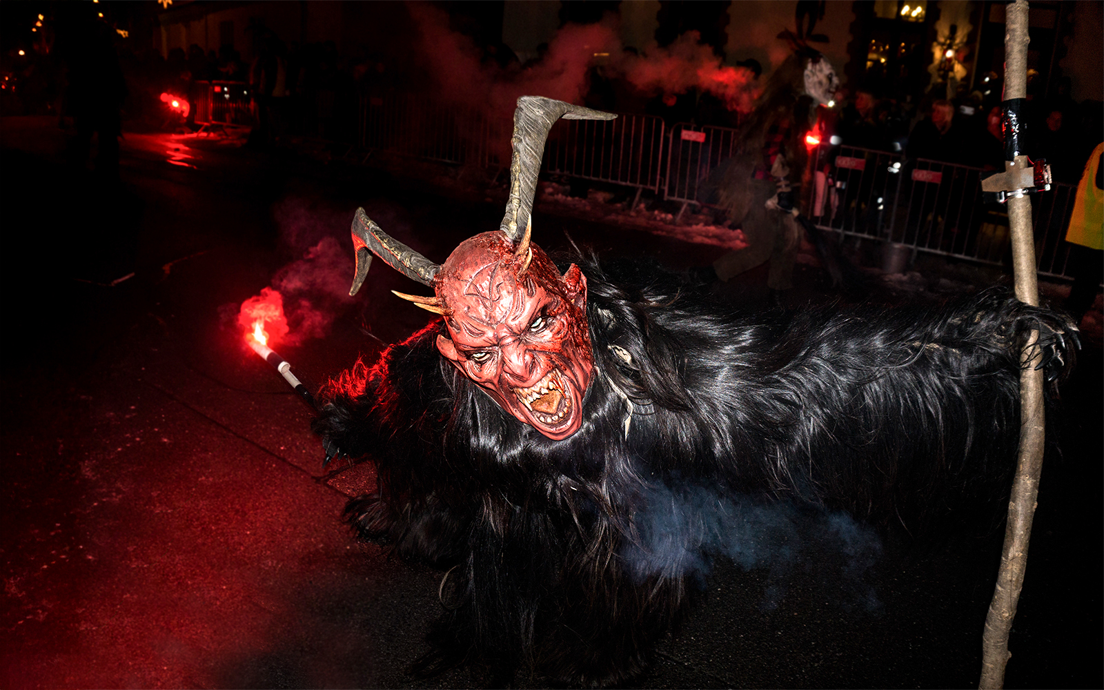 Person in a horned mask holding a torch during a Halloween parade.