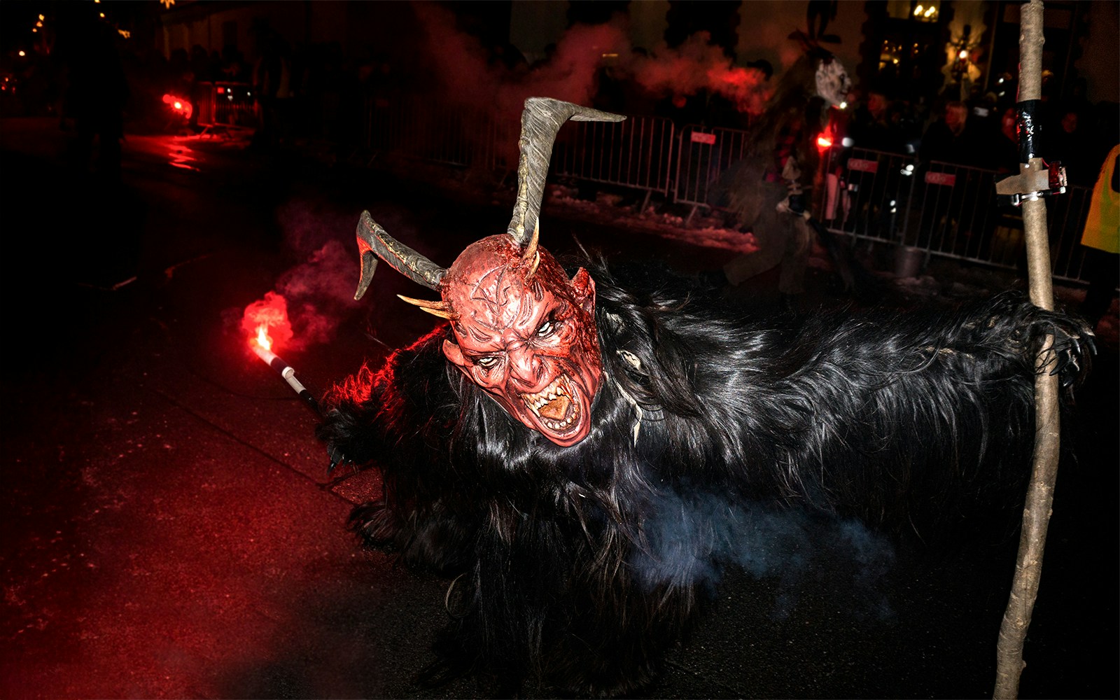 Person in a horned mask holding a torch during a Halloween parade.