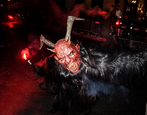 Person in a horned mask holding a torch during a Halloween parade.