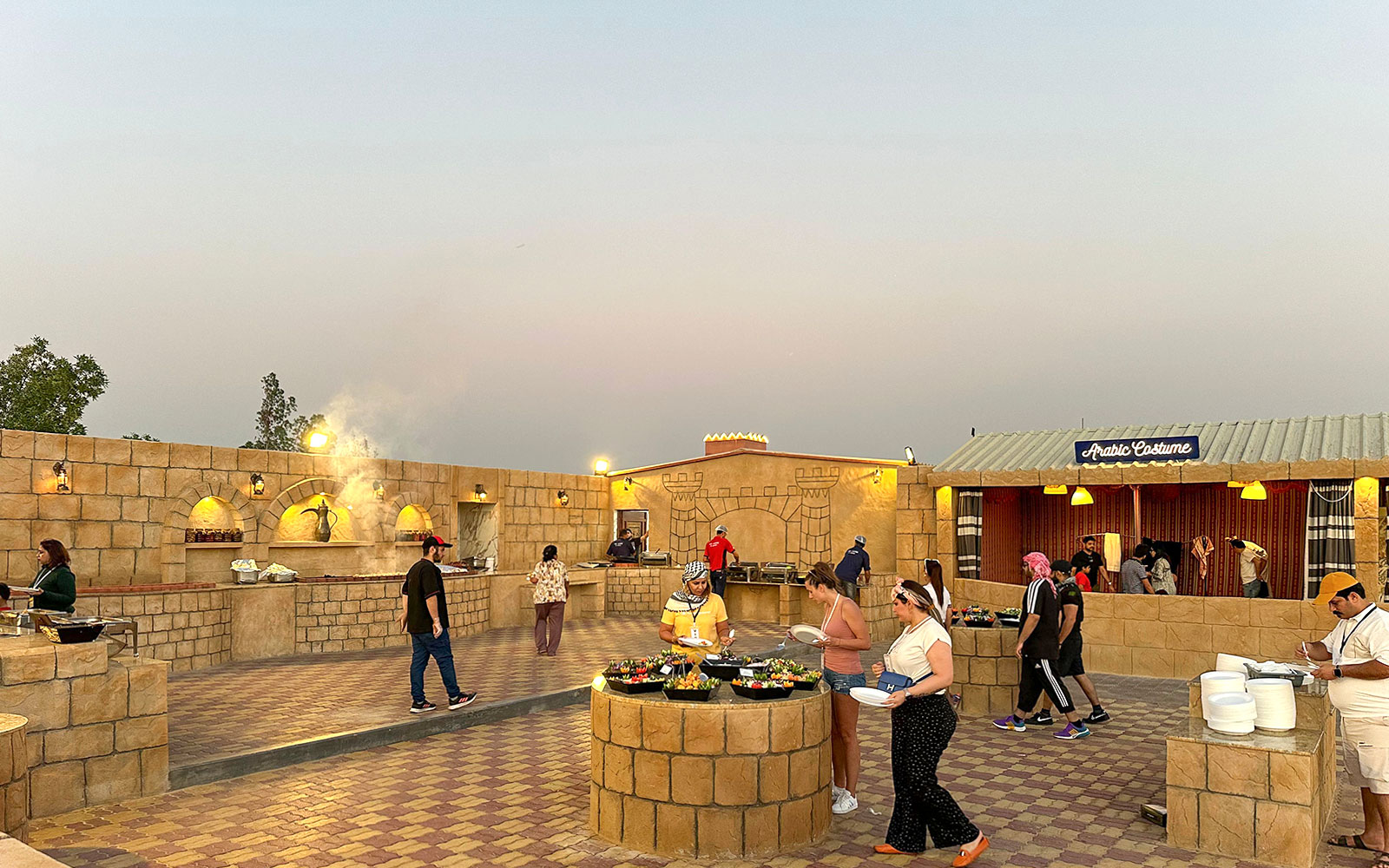 Guests enjoying buffet at an evening desert safari camp with Arabic decor.