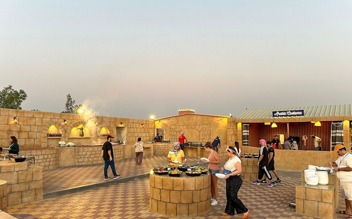 Guests enjoying buffet at an evening desert safari camp with Arabic decor.