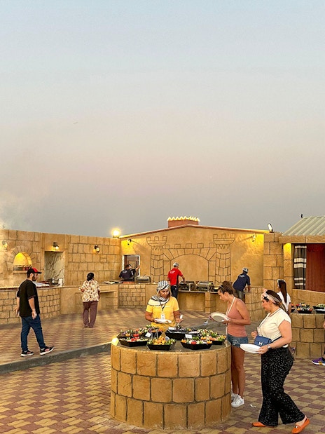Guests enjoying buffet at an evening desert safari camp with Arabic decor.