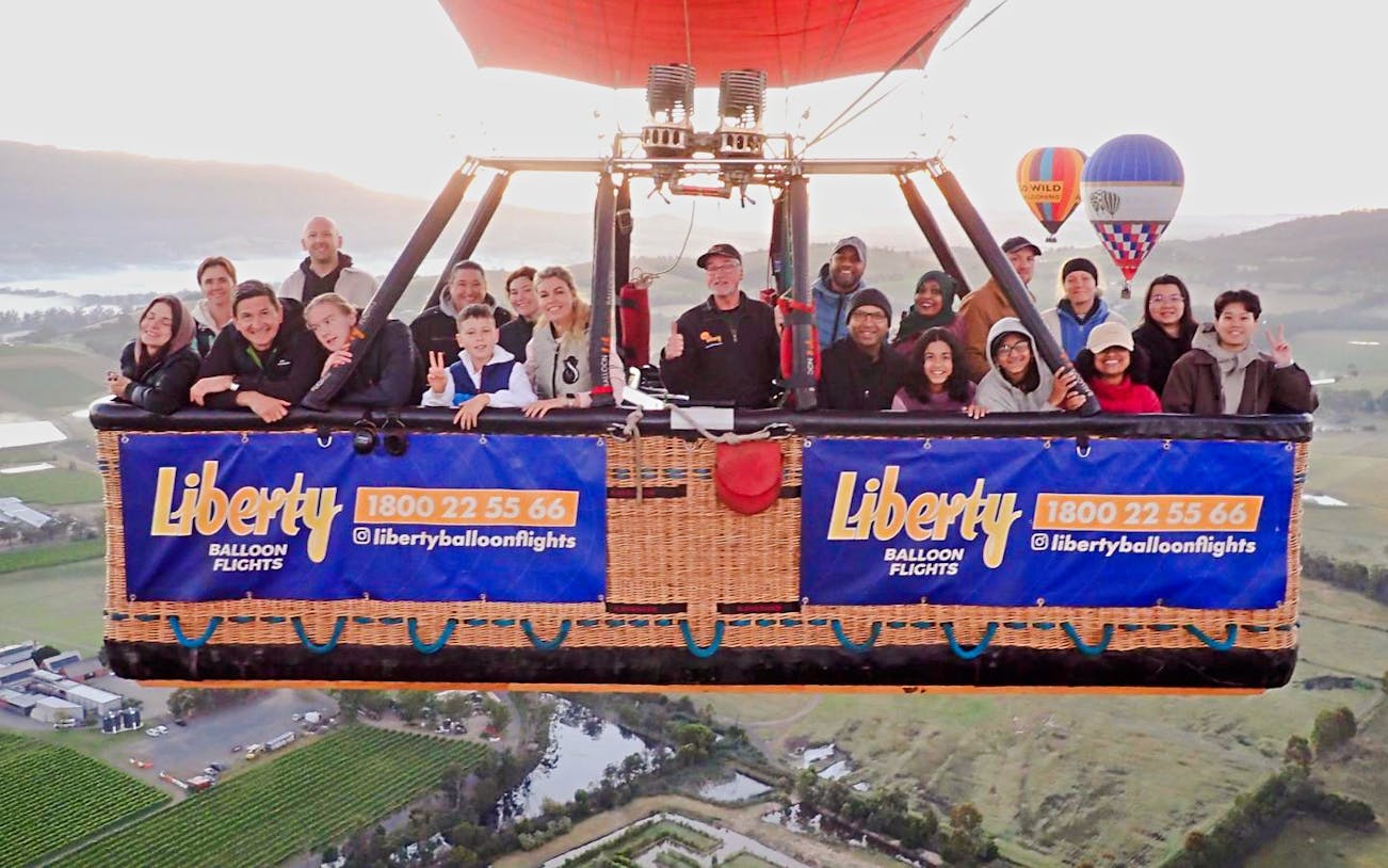 Hot air balloon ride with people over Yarra Valley, scenic landscape below.