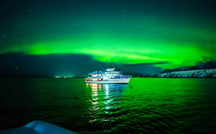 Boat under Northern Lights on a calm sea, Norway.