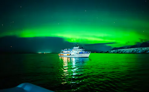 Boat under Northern Lights on a calm sea, Norway.