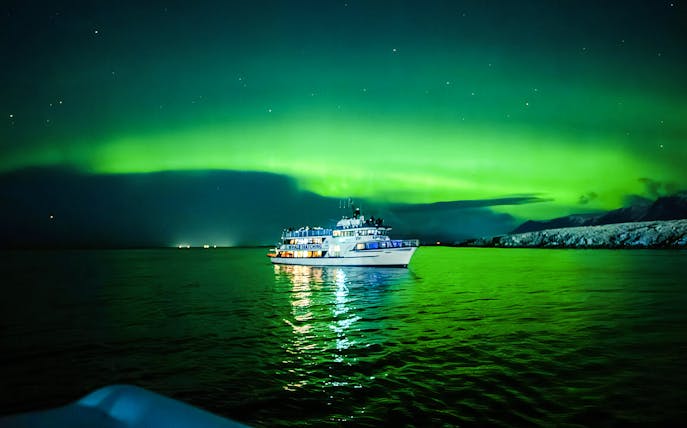 Boat under Northern Lights on a calm sea, Norway.
