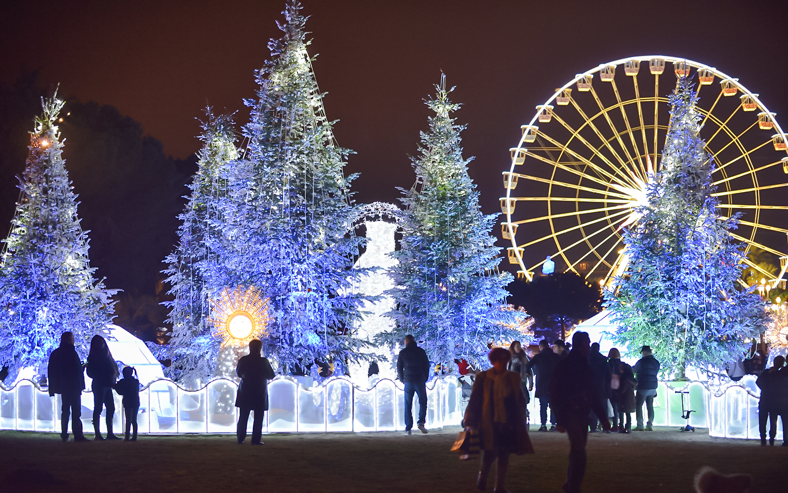 Christmas market in Nice with illuminated trees and Ferris wheel at night.