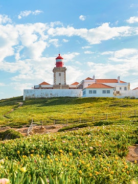 Cabo da Roca lighthouse with surrounding green landscape and blue sky.