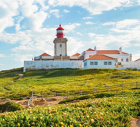 Cabo da Roca lighthouse with surrounding green landscape and blue sky.