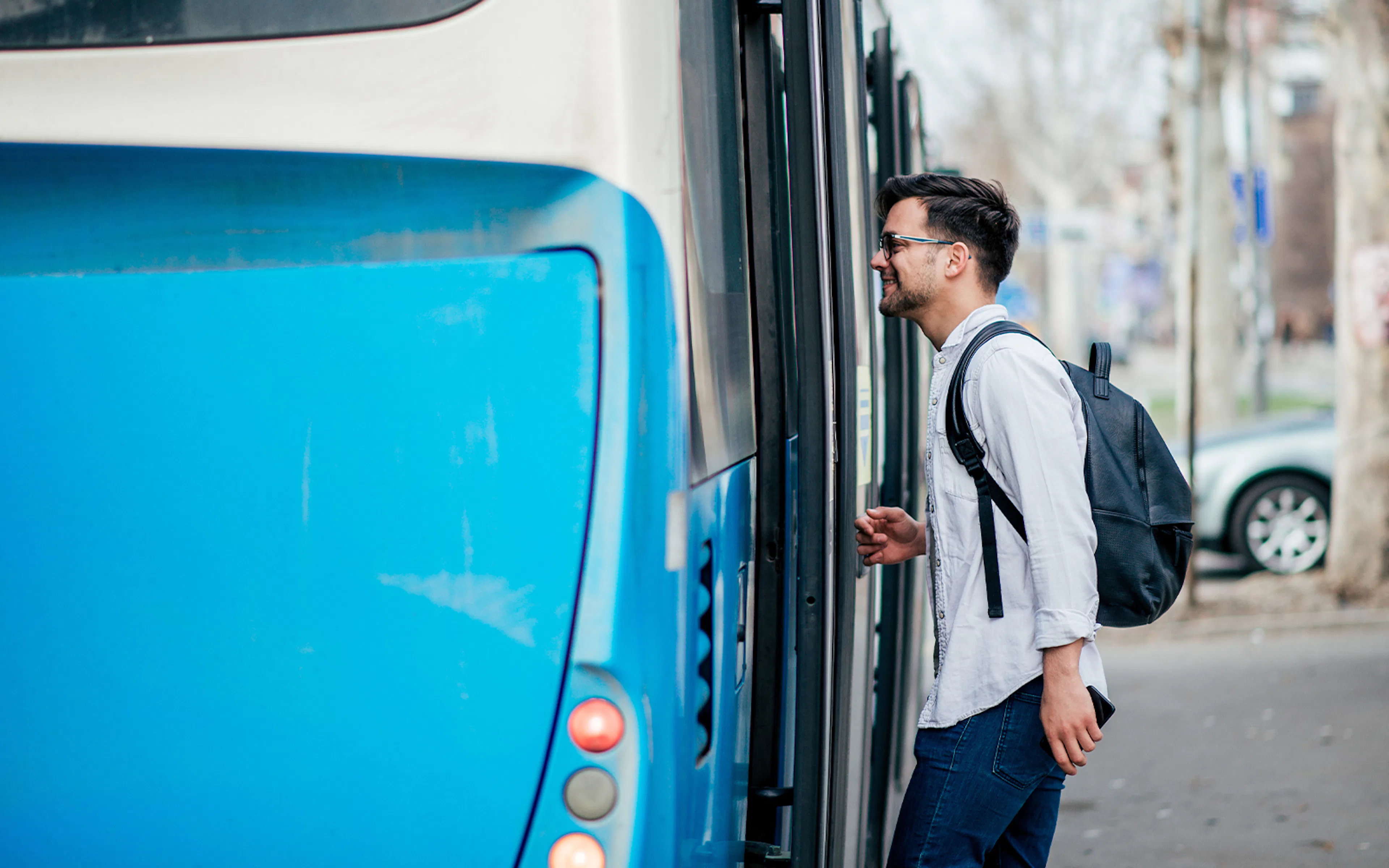 Man boarding a blue city bus with a backpack.