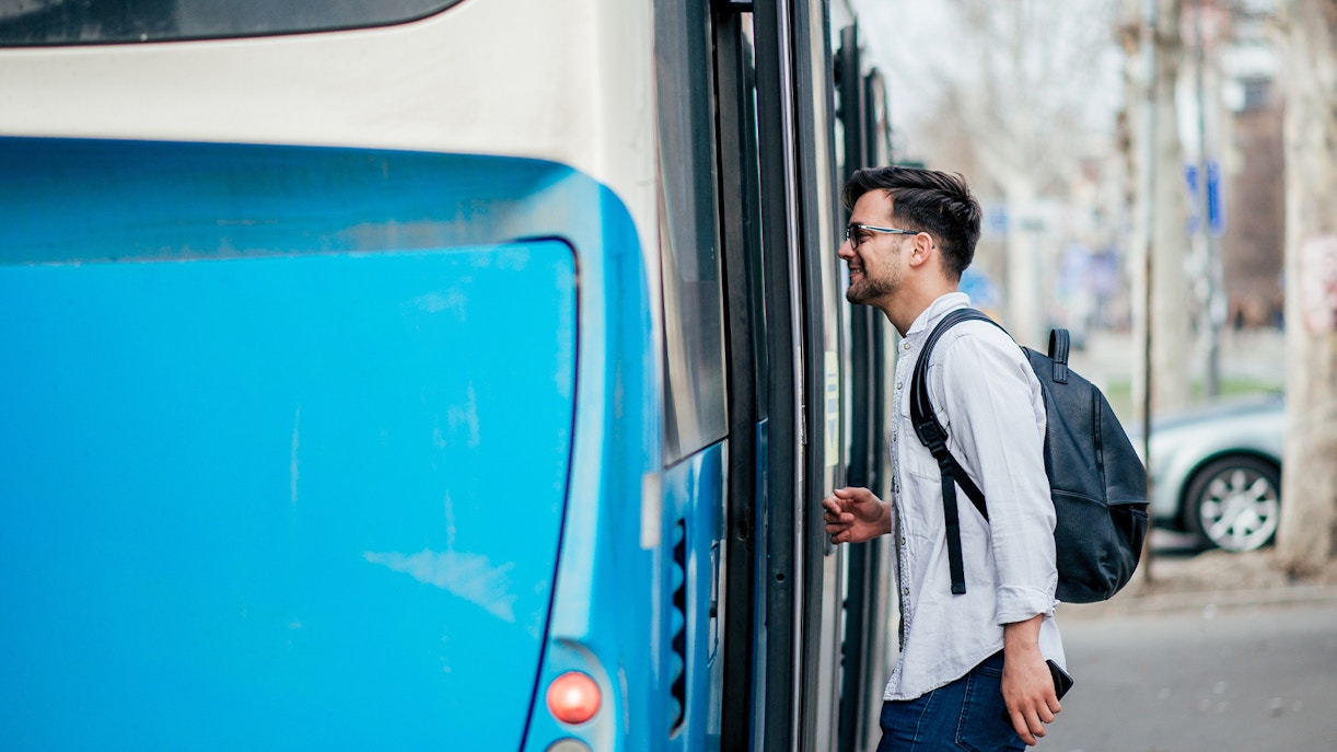 Man boarding a blue city bus with a backpack.