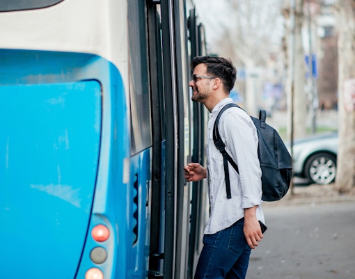 Man boarding a blue city bus with a backpack.