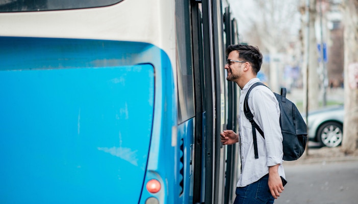 Man boarding a blue city bus with a backpack.