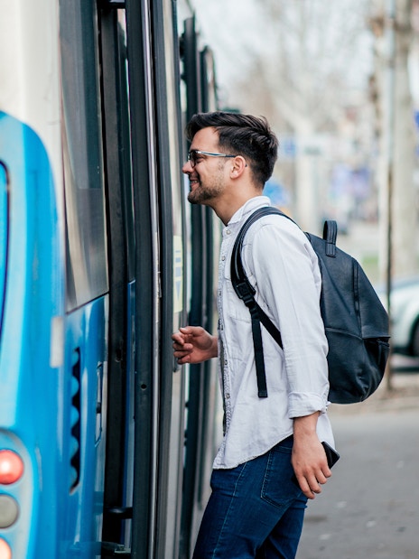 Man boarding a blue city bus with a backpack.