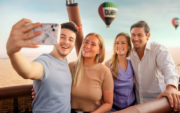 Group taking selfie in hot air balloon over Dubai desert at sunrise, part of premium overnight stay and heritage safari.