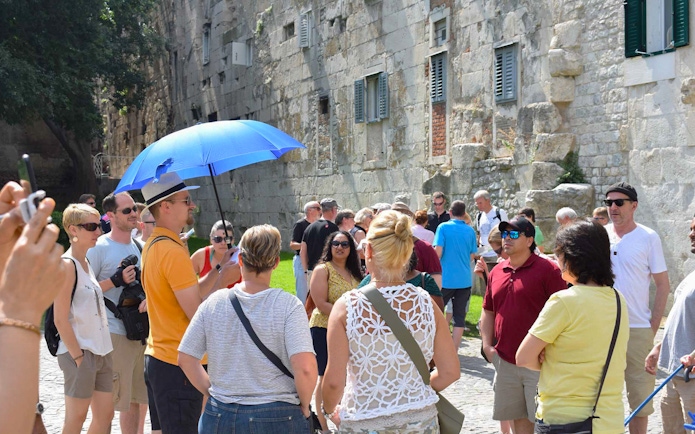 Tour group exploring Diocletian's Palace in Split with a guide holding a blue umbrella.