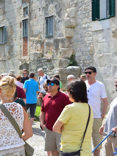 Tour group exploring Diocletian's Palace in Split with a guide holding a blue umbrella.