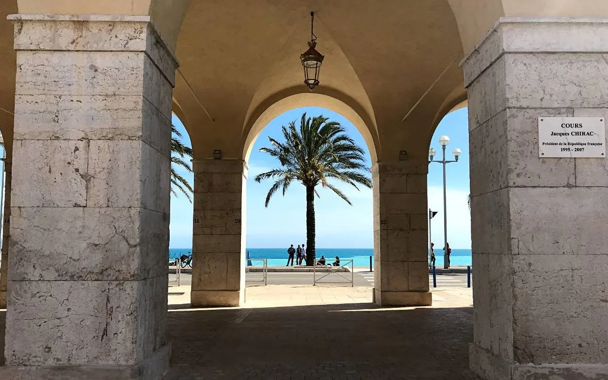 Arched walkway with palm tree and ocean view in Nice, France, part of self-guided city exploration game.